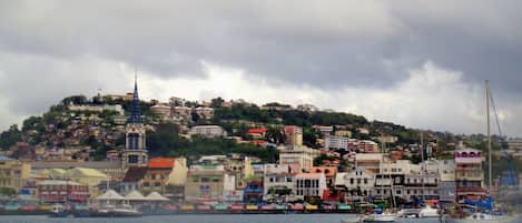Une ville côtière aux bâtiments aux couleurs vives, avec un clocher d’église imposant et des bateaux amarrés le long du quai.