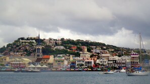 A coastal town with colorful buildings, a prominent church spire, and boats docked along the waterfront.