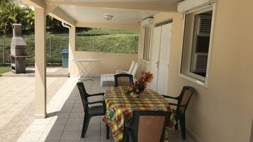 Une terrasse couverte avec une table dressée pour deux personnes, entourée de chaises, d’un barbecue et offrant une vue sur un paysage verdoyant.
