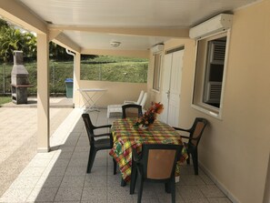 Une terrasse couverte avec une table dressée pour deux personnes, entourée de chaises, d’un barbecue et offrant une vue sur un paysage verdoyant.