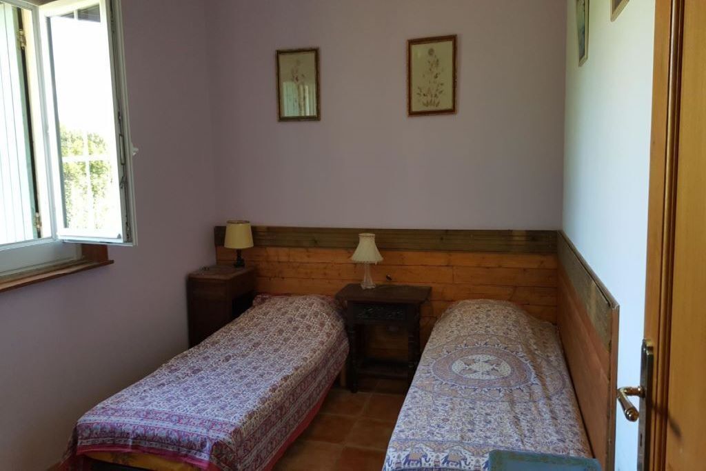 A small room with two single beds, a wooden headboard, a nightstand with a lamp, and a window with blinds.