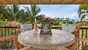 Une table ronde entourée de chaises, une bouteille de champagne et un verre, le tout sur une terrasse couverte d’où l’on peut admirer une maison et des palmiers.