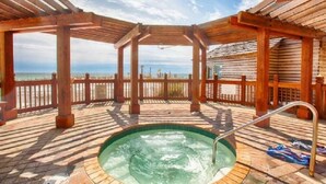 Un mirador de madera con jacuzzi y vista a la playa.