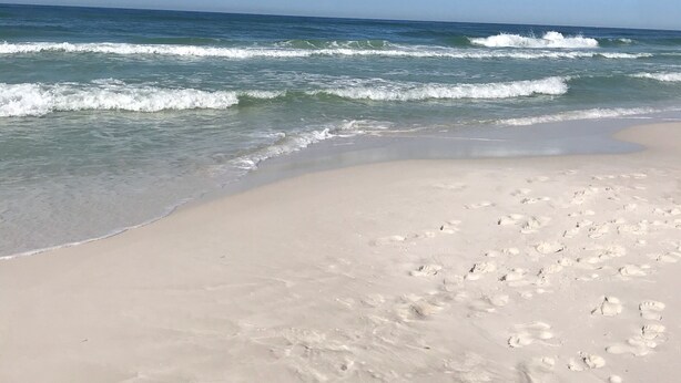 Una playa con huellas en la arena y olas rompiendo en la orilla.