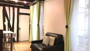 A modern living room with a black leather sofa, a small white table, and green curtains. - Charming studio Ile Saint Louis PARIS 4 ° ° - Paris (Paris)