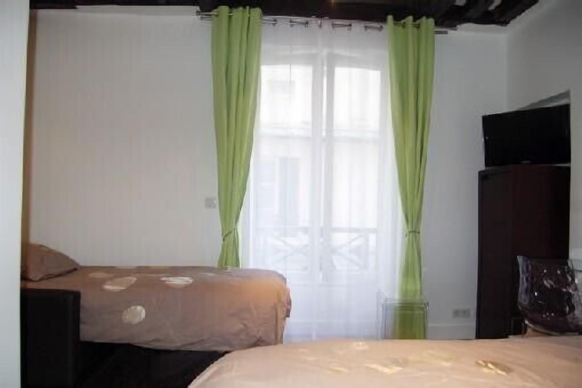 Une chambre avec deux lits, une télévision et une fenêtre avec des rideaux verts.