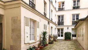 A narrow cobblestone courtyard with potted plants and a building with white shutters and balconies. - Charming studio Ile Saint Louis PARIS 4 ° ° - Paris (Paris)