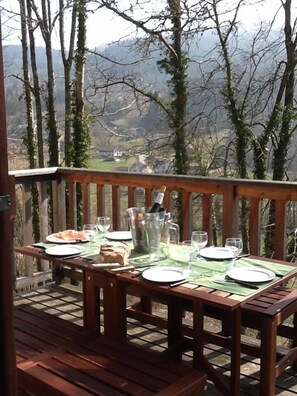 Une terrasse en bois avec une table dressée pour un repas, offrant une vue sur un paysage montagneux.