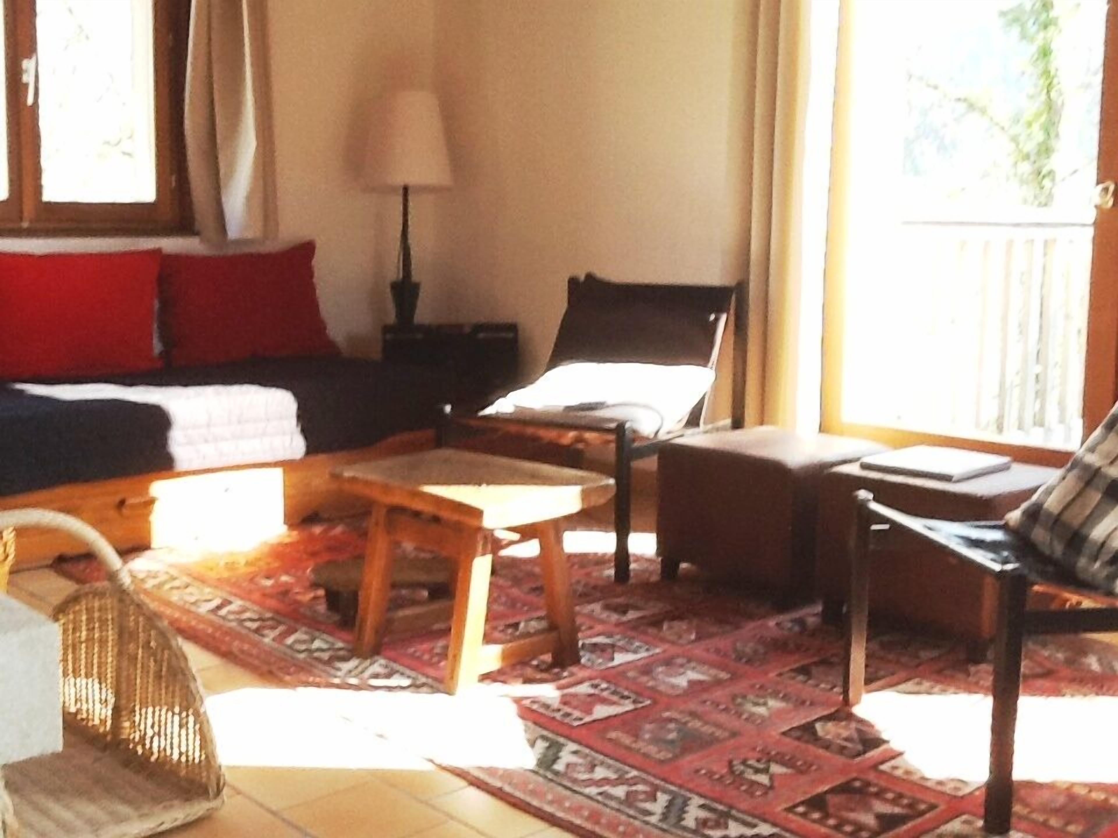 A cozy living room with a sofa, a wooden coffee table, and a chair. There is a window with curtains, a lamp, and a rug on the floor.