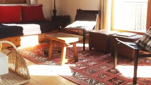 A cozy living room with a sofa, a wooden coffee table, and a chair. There is a window with curtains, a lamp, and a rug on the floor. - Gérardmer, superb valley view, Gite ****, Internet, TV, Short Stay adm (Rochesson)