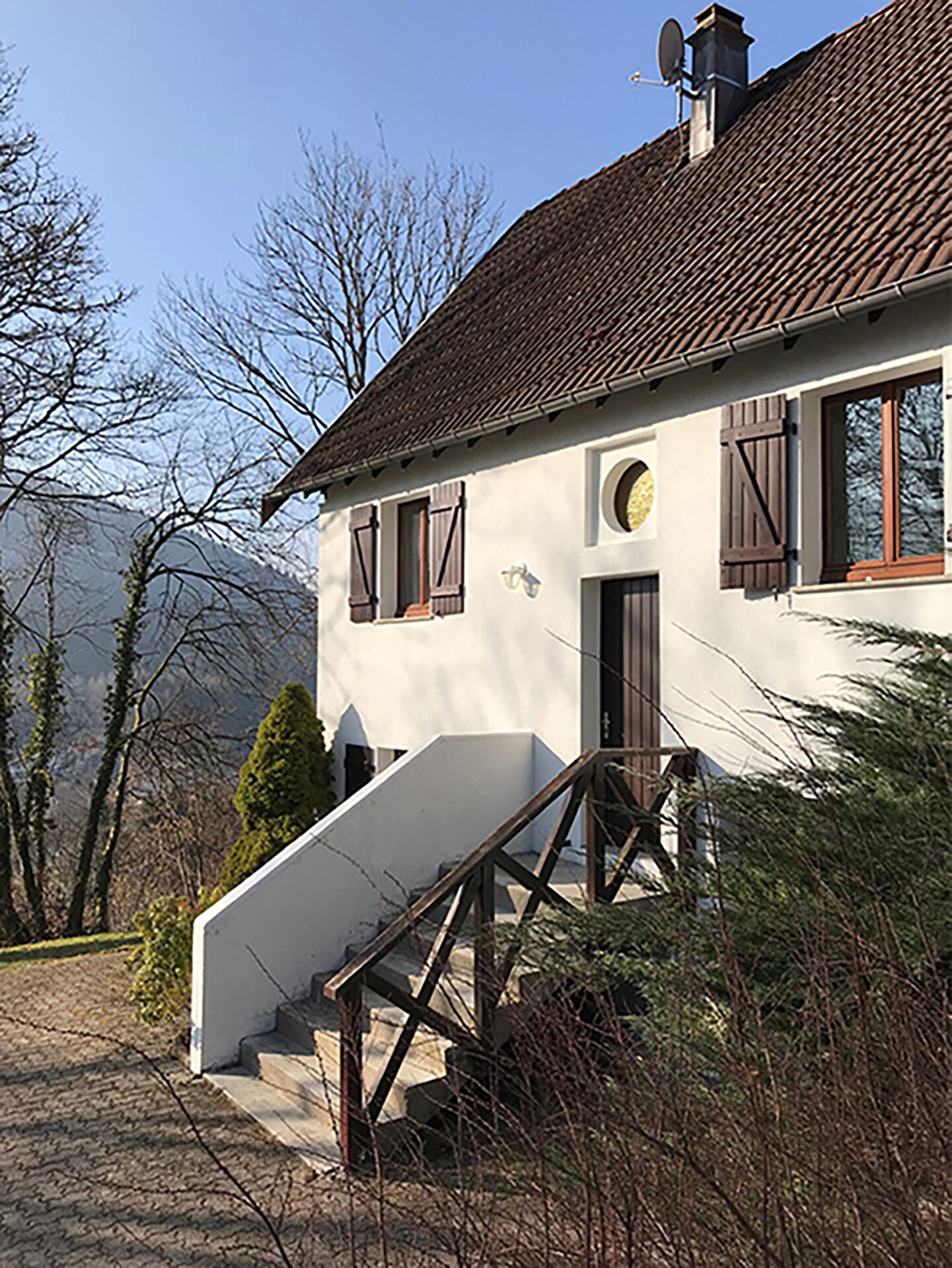 A house with a steep staircase leading to a door, surrounded by trees and hills.