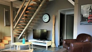 Ein modernes Wohnzimmer mit Treppe, Flachbildfernseher, Ledersofa und einer Wanduhr.