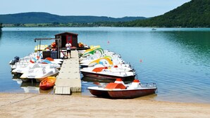 Ein Steg mit mehreren kleinen Booten, ein kleines Gebäude und ein See mit Hügeln im Hintergrund.