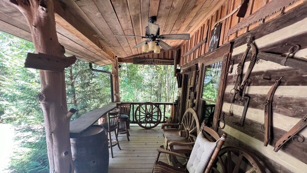 Uma cabana de madeira com varanda, cadeiras de balanço, uma mesa e um ventilador de teto.