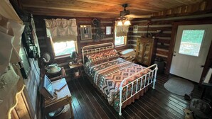 Um quarto de cabana aconchegante, com uma cama de madeira, uma mesinha de cabeceira, um penteado e uma janela com cortinas.