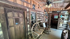 Um interior rústico com uma porta de madeira identificada com a palavra 'Cowboy', uma carroça antiga e um ventilador de teto.