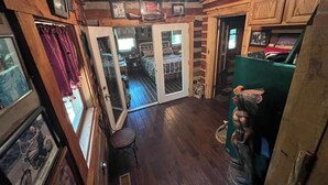 Quarto rústico com paredes e teto de madeira, porta de vidro deslizante para um quarto, um banquinho pequeno e um sofá verde.