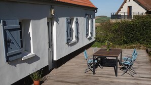 A white building with a balcony, a wooden deck, and a table with chairs.