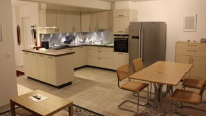 Une cuisine moderne avec un coin repas, dotée de meubles de couleur claire, d’appareils électroménagers en acier inoxydable et d’un îlot central.
