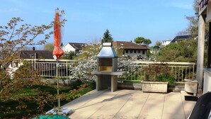 Une terrasse avec un barbecue, un pot de fleurs et une clôture en métal.