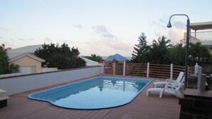 Ein Swimmingpool mit einer Holzterrasse, weißen Liegestühlen und Blick auf einen Berg im Hintergrund.