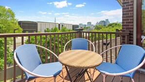 A balcony with two blue wicker chairs and a small round table, overlooking a cityscape with modern buildings and greenery. - 1.0 mile to Broadway, 1.2mi Topgolf, 1.4mi Music City Center, 2.4mi Vanderbilt (Nashville)