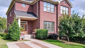 A two-story brick house with a front porch, a garage, and a well-maintained lawn. - 1.0 mile to Broadway, 1.2mi Topgolf, 1.4mi Music City Center, 2.4mi Vanderbilt (Nashville)
