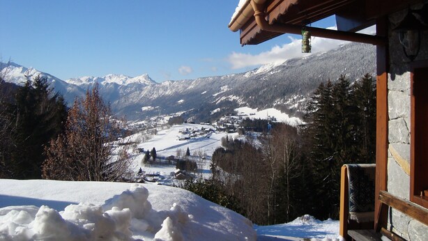Eine verschneite Berglandschaft mit einer Holzhütte und Blick auf ein Dorf darunter.