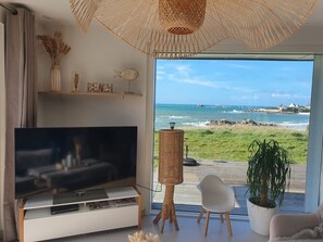 A modern living room with a large TV, wicker furniture, and a view of the beach. - Villa des Courlis, 10 people, beach at your feet (Kerlouan)