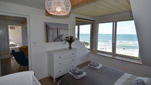 A bedroom with a bed, a dresser, a chair, and a large window with a view of the ocean. - Villa des Courlis, 10 people, beach at your feet (Kerlouan)