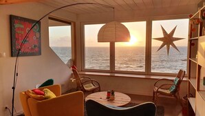 A cozy living room with a view of the sea at sunset, featuring a round table, two chairs, and a star decoration on the wall. - Villa des Courlis, 10 people, beach at your feet (Kerlouan)