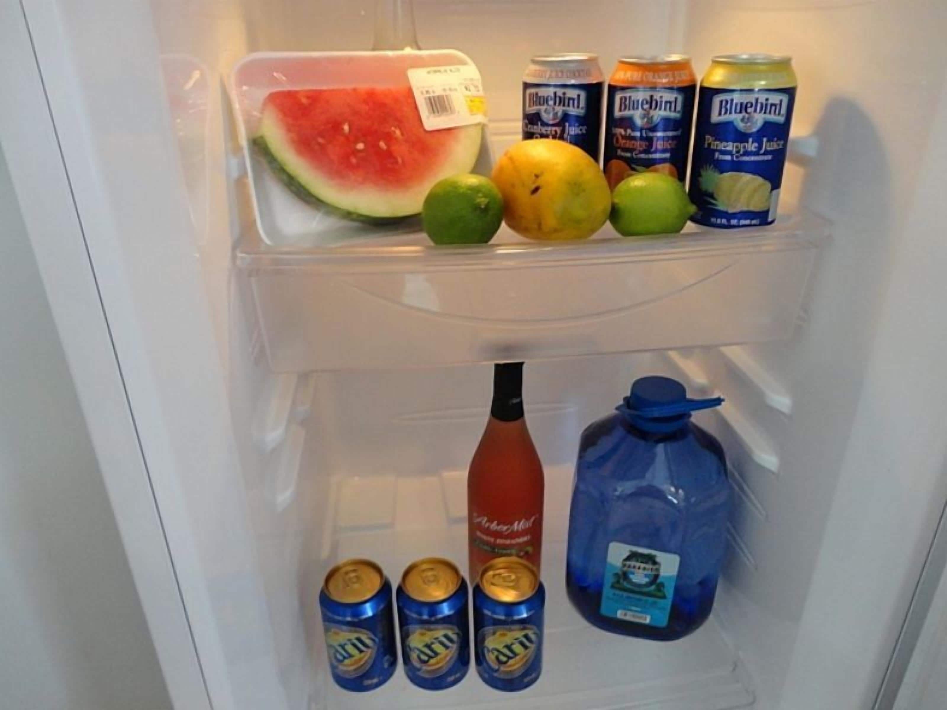 A refrigerator with a watermelon, limes, and cans of Bluebell and Dr. Martens beverages.