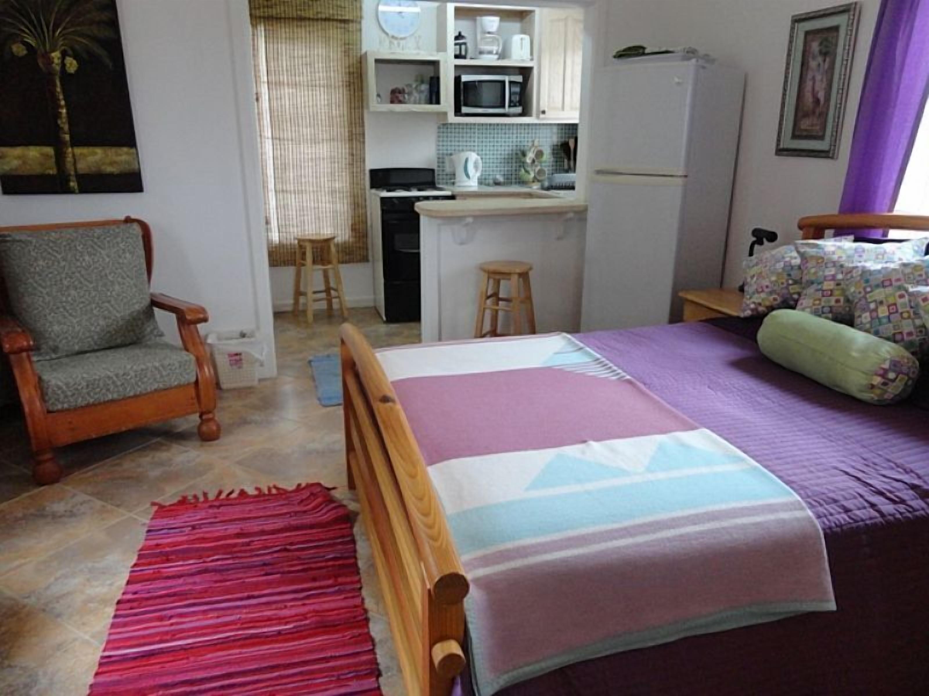A bedroom with a bed, a chair, a kitchen area, and a bathroom.