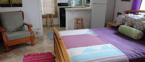 A bedroom with a bed, a chair, a kitchen area, and a bathroom.