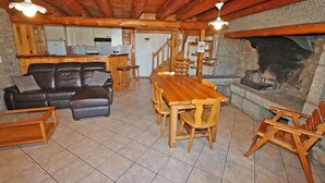 Ein gemütliches Wohnzimmer mit Esstisch aus Holz, einer Ledersofa und einem Kamin aus Stein.