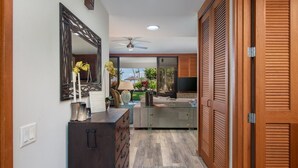 A hallway with a dark wooden cabinet, a glass coffee table, and a mirror. - Prime Location, Unit H-102, Oceanfront next to pool. (Kamuela)