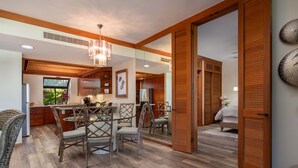 A spacious kitchen with wooden flooring, a dining area with wicker chairs, and a large window. - Prime Location, Unit H-102, Oceanfront next to pool. (Kamuela)