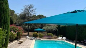 Piscina com espreguiçadeiras e guarda-sóis, cercada por vegetação.