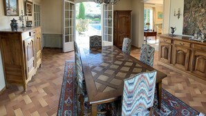 Uma sala de jantar espaçosa com uma grande mesa de madeira, cadeiras estampadas e vista para o exterior através de uma porta aberta.