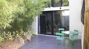 Un patio moderno con puerta de vidrio, sillas verdes y una planta de bambú.