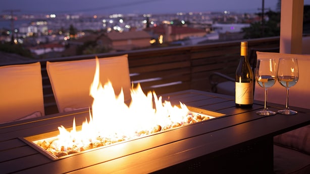 A wooden table with a built-in fire feature, two wine glasses, and a bottle of wine.