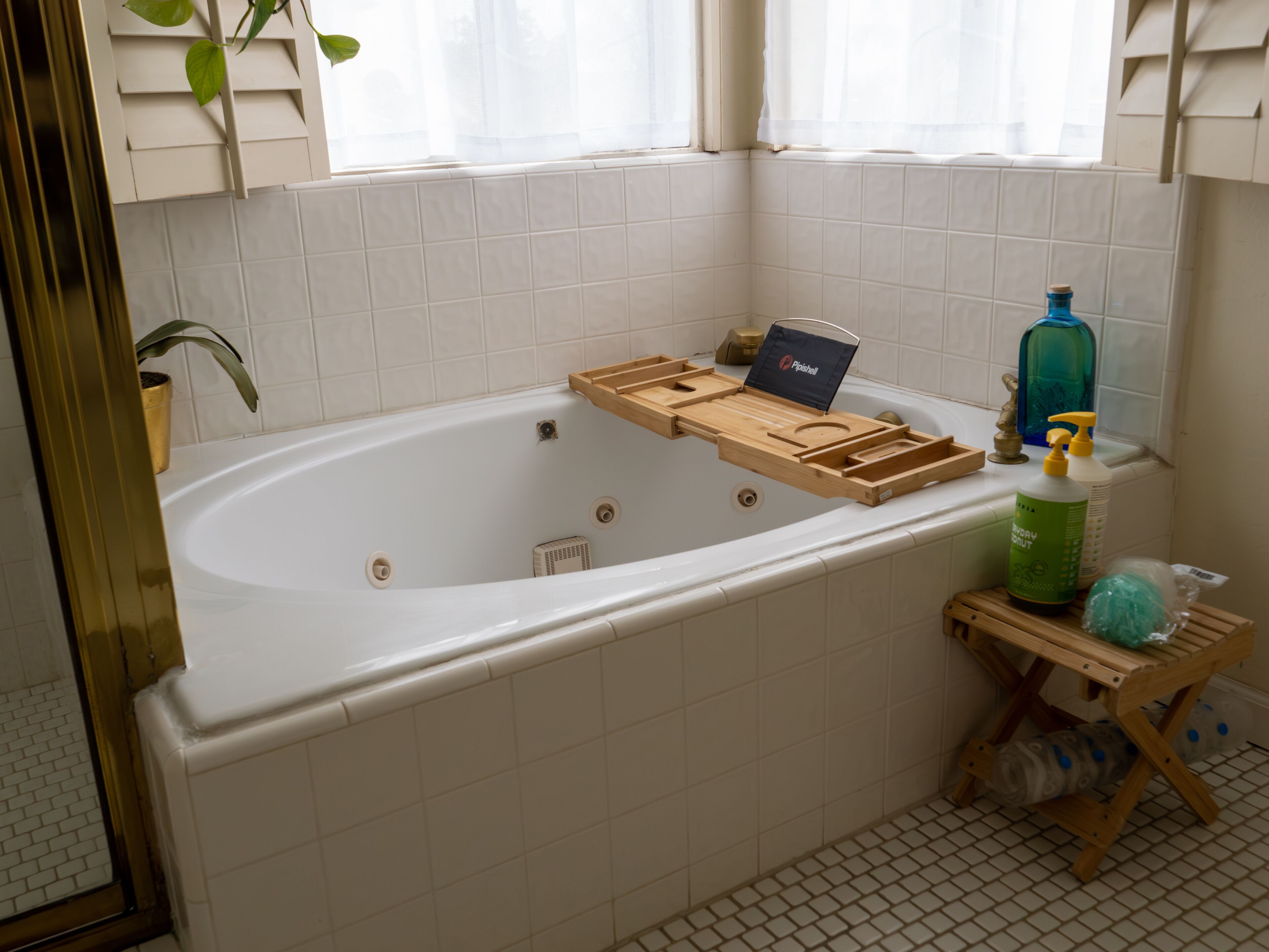 A bathroom with a bathtub, a wooden tray, a bottle of shampoo, and a small stool.