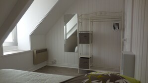 Un dormitorio con techo inclinado, una cama con almohada verde y marrón, un armario blanco y una ventana.