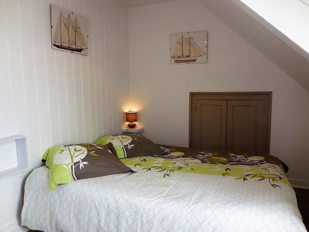 A bedroom with a bed, a nightstand with a lamp, and two wall-mounted paintings of sailboats.