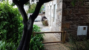 Un edificio de piedra con una verja de madera, rodeado de abundante vegetación y un camino de grava.