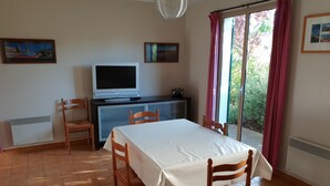 Een kamer met een eettafel, stoelen, een televisie en een schuifdeur naar een tuin.