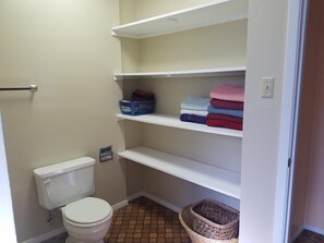 A small bathroom with a toilet, shelves for storage, and a basket on the floor. - The Pines at Mayhill (Mayhill)