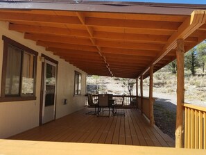 A covered outdoor area with a table and chairs, a door, and a view of the surrounding landscape. - The Pines at Mayhill (Mayhill)