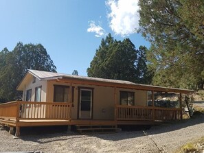 A single-story cabin with a wooden deck, a front door, and a small porch. - The Pines at Mayhill (Mayhill)