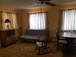 A living room with a sofa, a rocking chair, a dining table, and a ceiling fan. - The Pines at Mayhill (Mayhill)